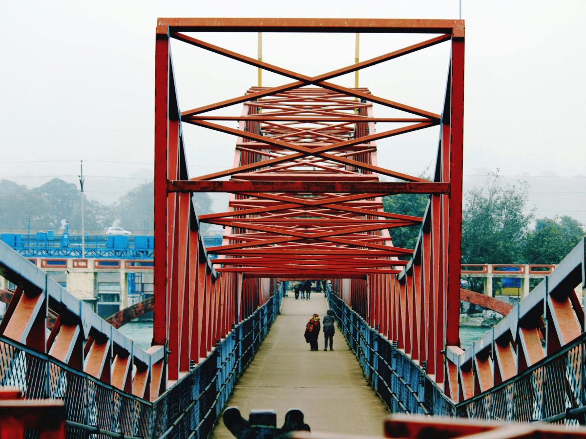 People walking across a red steel bridge in Haridwar, India, showcasing modern infrastructure.